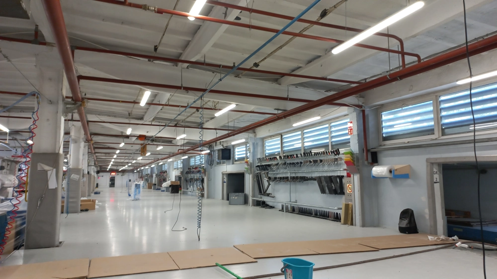 Hala przemysłowa z podwieszonymi oprawami LED i zwisającymi przewodami podczas Montaż oświetlenia