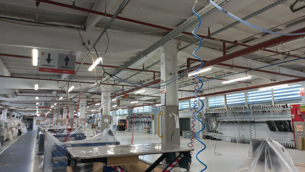Montaż oświetlenia LED w dużej hali przemysłowej z zawieszonymi oprawami i przewodami instalacyjnymi
