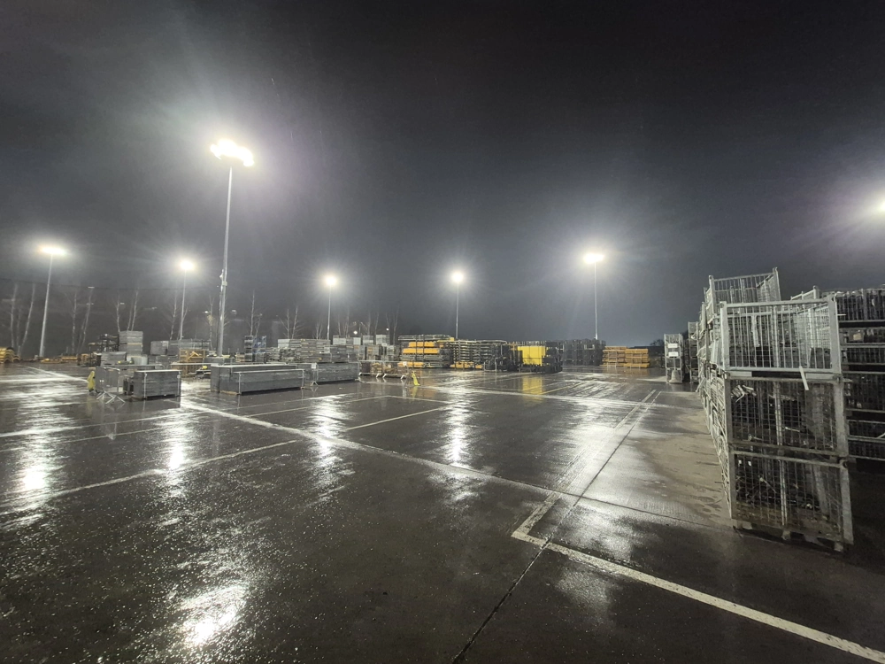 Plac magazynowy z paletami i regałami oświetlony naświetlaczami led rozmieszczonymi na wysokich masztach
