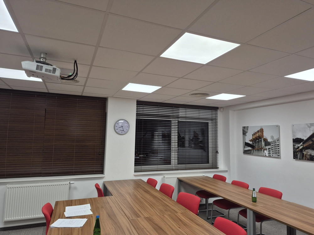 Sala szkoleniowa z sufitowymi panelami LED, drewnianymi stołami, czerwonymi krzesłami i projektorem – Oświetlenie biurowe