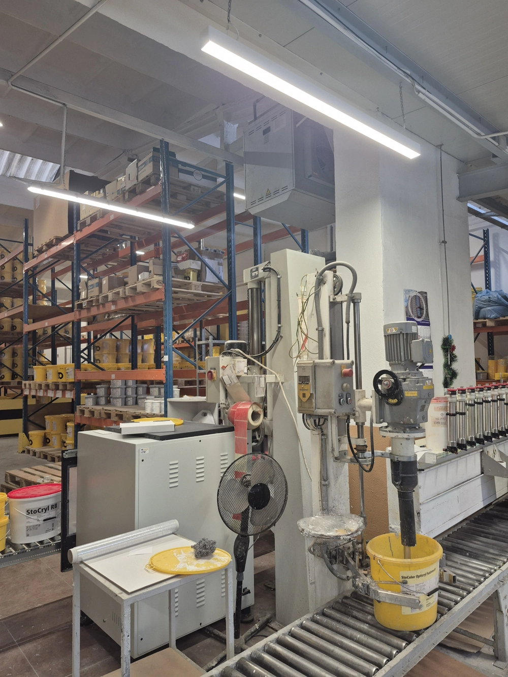 Mieszarka przemysłowa przy regałach w magazynie oświetlonym liniowymi lampami do hali produkcyjnej