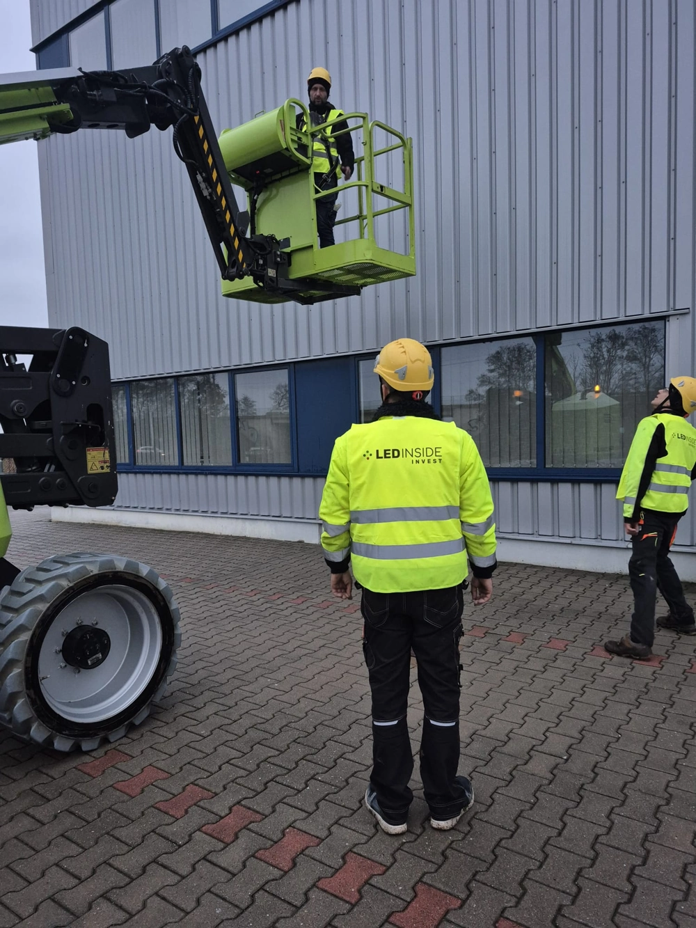 Pracownicy podczas montaż oświetlenia na elewacji budynku z użyciem podnośnika