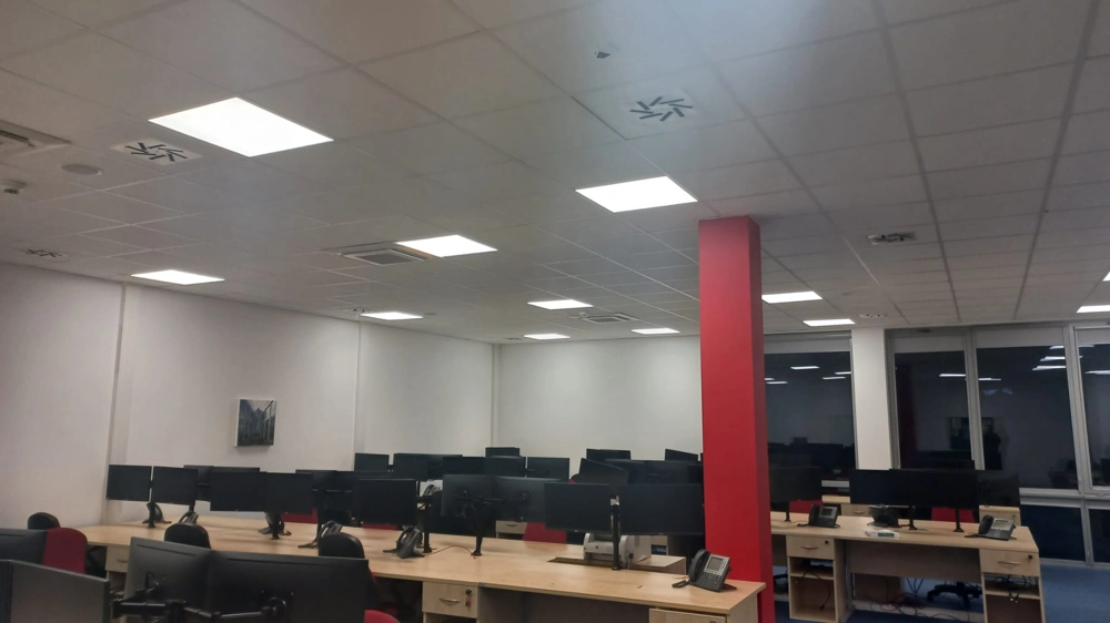 Widok biura z sufitowymi panelami LED i stanowiskami komputerowymi – oświetlenie biurowe
