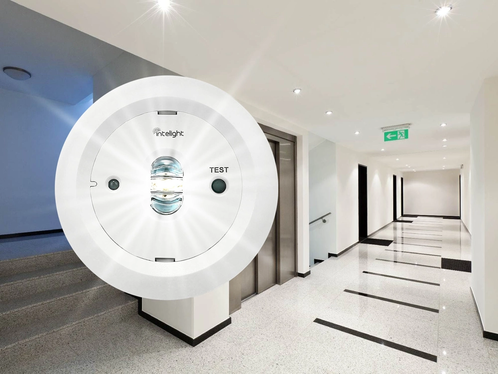 Oświetlenie awaryjne LED z przyciskiem TEST zamontowane w białym korytarzu biurowym z oprawami sufitowymi