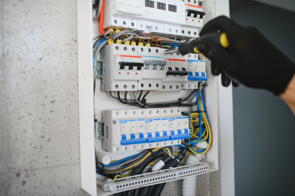 Elektryk w czarnych rękawicach montujący rozdzielnice elektryczne z bezpiecznikami i przewodami