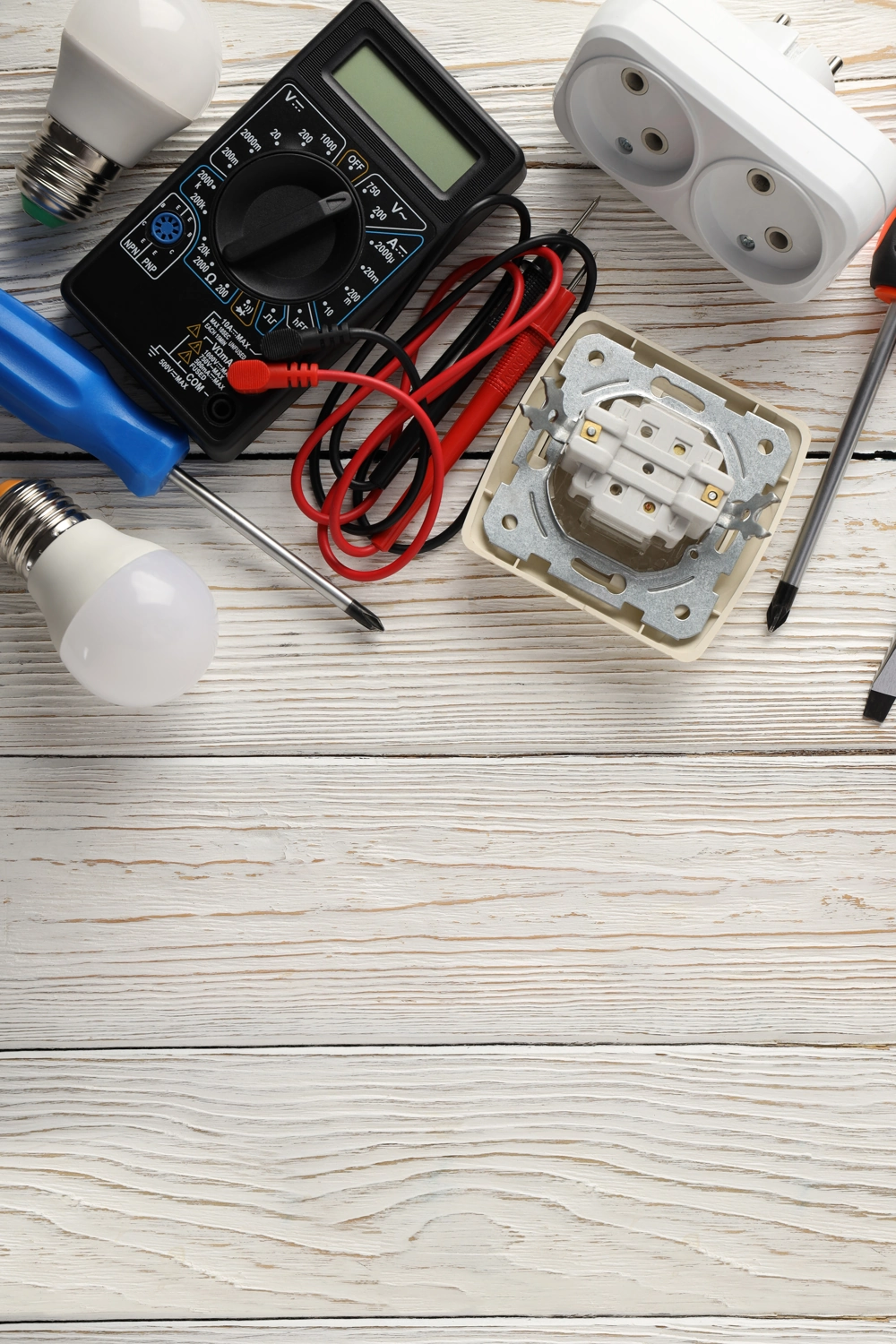 Multimetr i żarówki LED na drewnianym blacie, obok gniazdko i narzędzia przygotowane do Pomiar natężenia oświetlenia