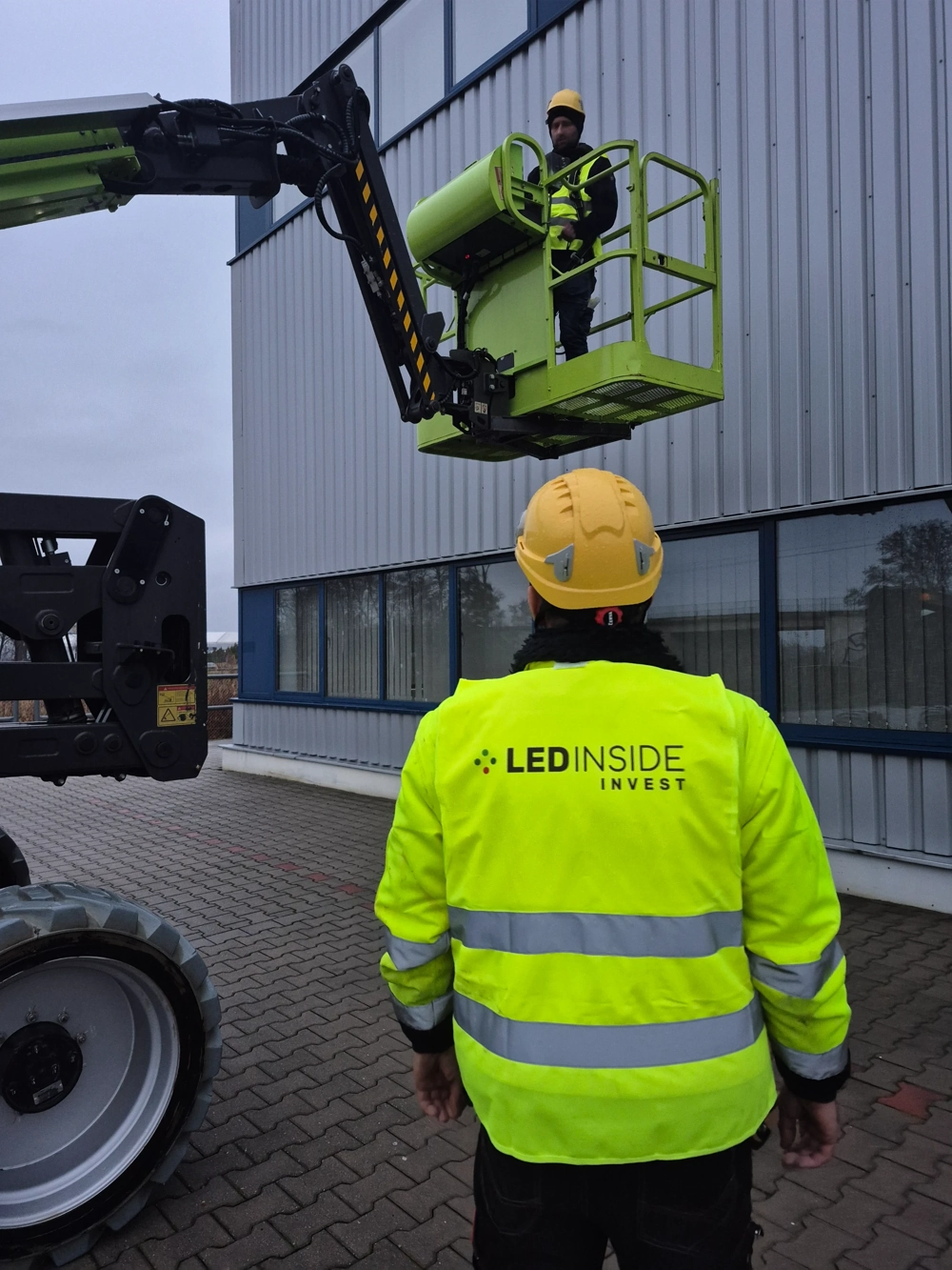 Pracownik nadzorujący montaż oświetlenia z platformy podnośnika na zewnątrz budynku