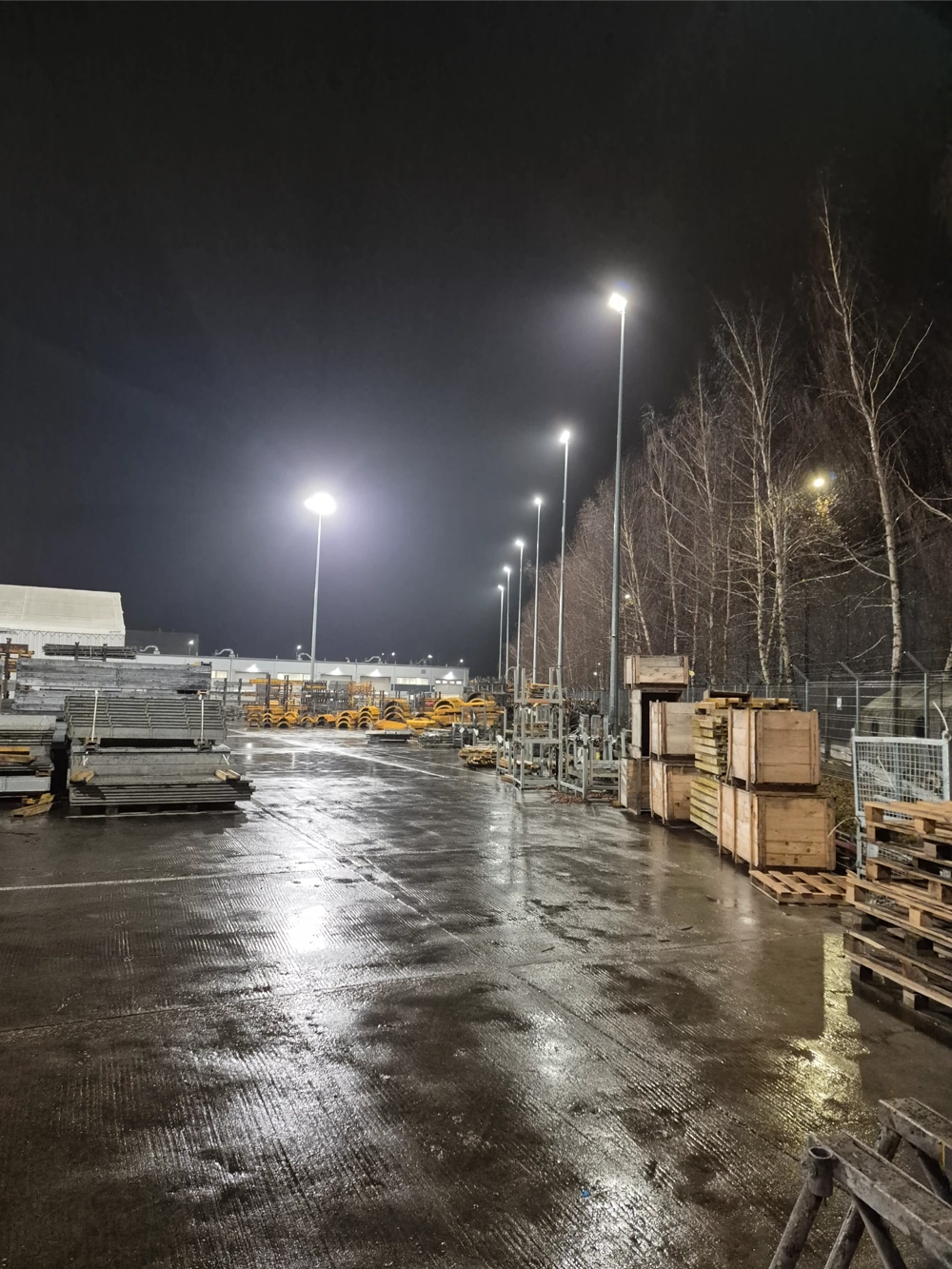 Plac magazynowy z regałami i paletami oświetlony wysokimi słupami LED – oświetlenie zewnętrzne
