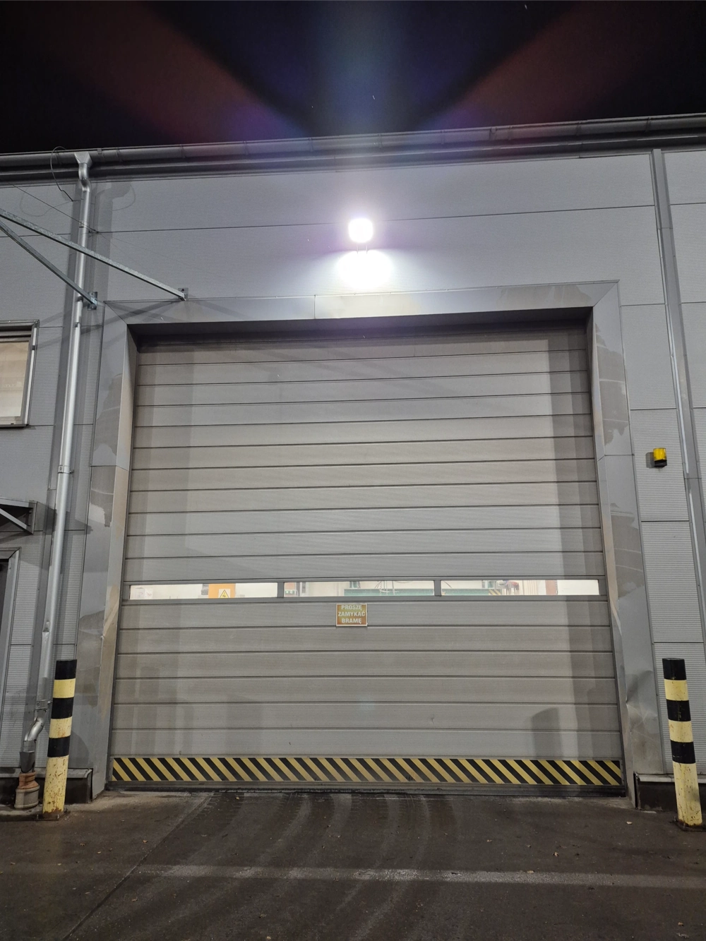 Naświetlacze led oświetlają zewnętrzne drzwi przemysłowej hali i przestrzeń przed nimi