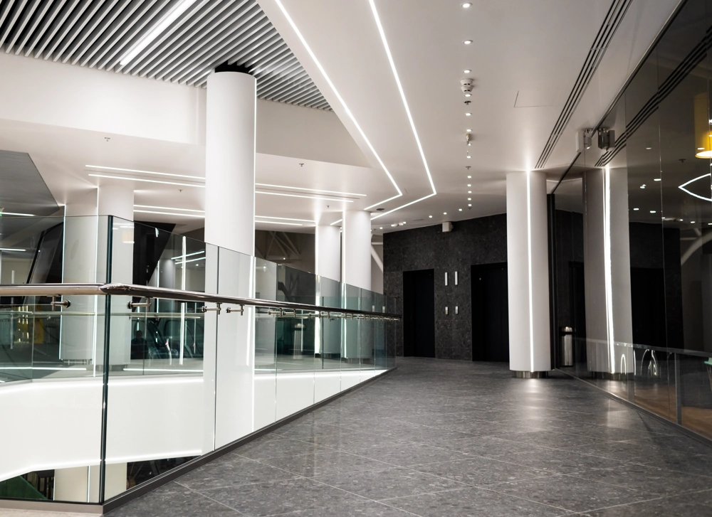 Wnętrze korytarza z białymi kolumnami, szklanym balustradą i sufitowym oświetleniem LED – Oświetlenie biurowe