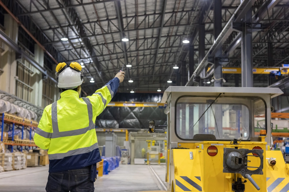 Technik w odblaskowej kamizelce i kasku kierujący ruchem wewnątrz hali magazynowej z oświetleniem LED