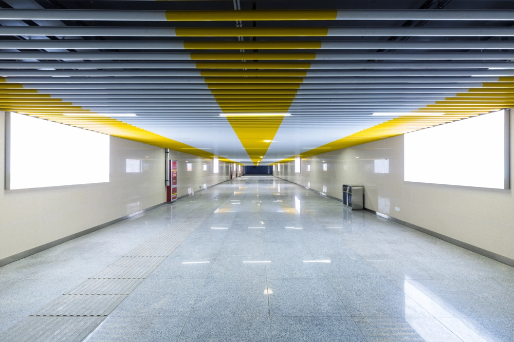 Długi korytarz z żółto-szarym sufitem i sufitowymi oprawami oświetleniowymi LED Oprawy oświetleniowe